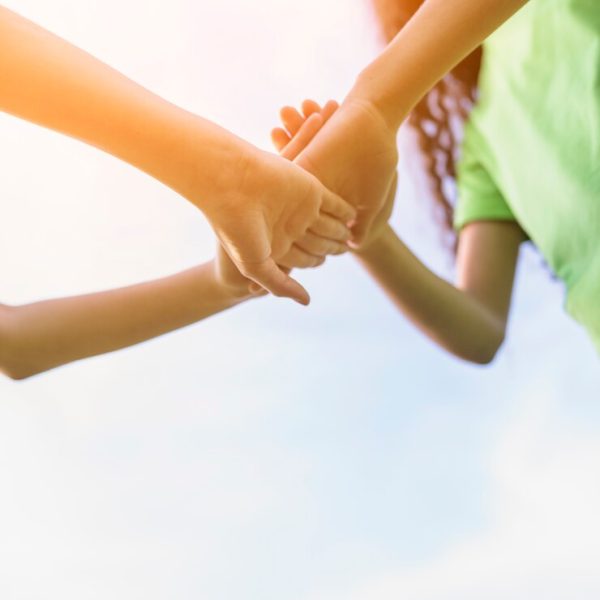 happy-girls-stacking-their-hands-playing-against-sky